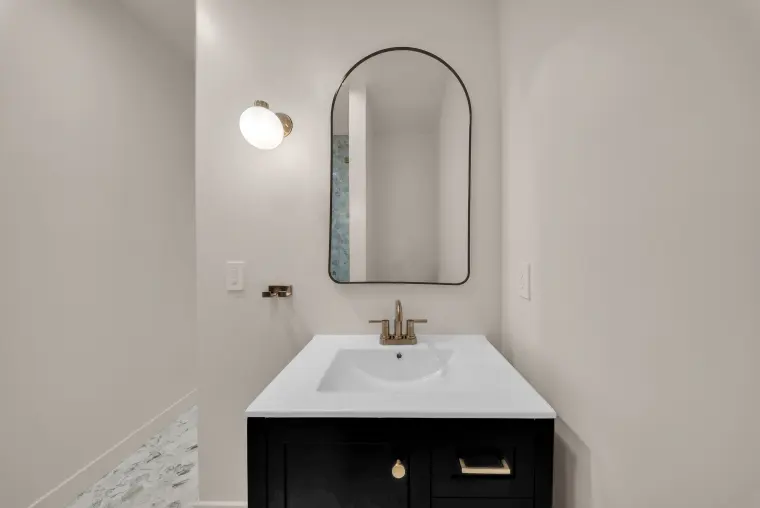 Powder room with a black vanity, brass faucet, arched black-framed mirror, and a globe wall sconce