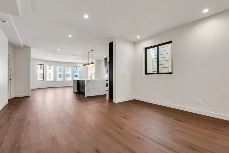 Open living and kitchen space with a bay window at the far end, a waterfall quartz island, and wide-plank flooring