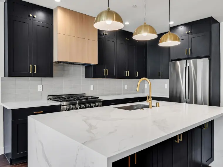Close-up of finished kitchen with black shaker cabinets, light wood range hood, brass pendants, gas range, and waterfall quartz island