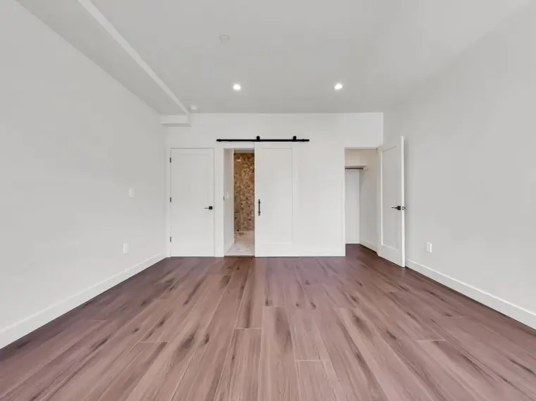 Empty finished primary bedroom with black sliding barn door to ensuite bathroom, walk-in closet, and wood flooring