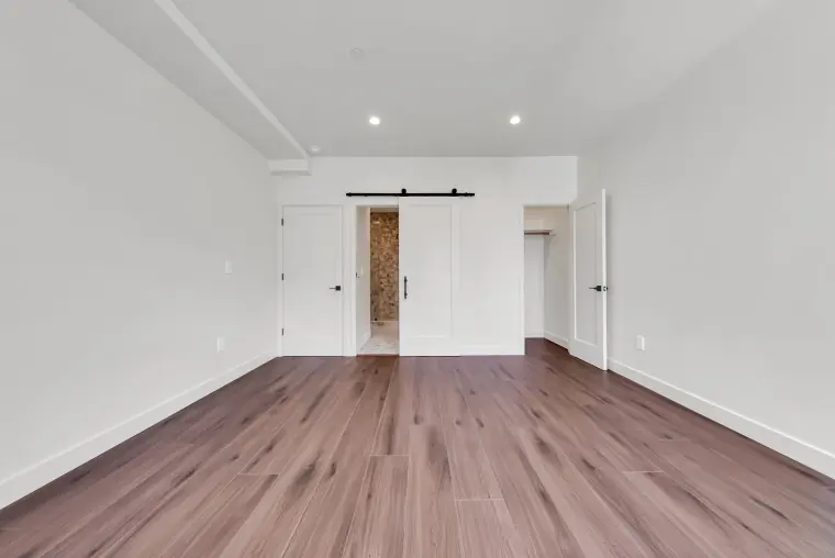 Primary bedroom with a black-hardware sliding barn door to the ensuite bathroom, a closet, and wood flooring
