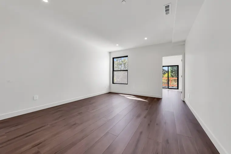 Bedroom with wood flooring, a black-framed window, and a doorway to a deck with trees beyond