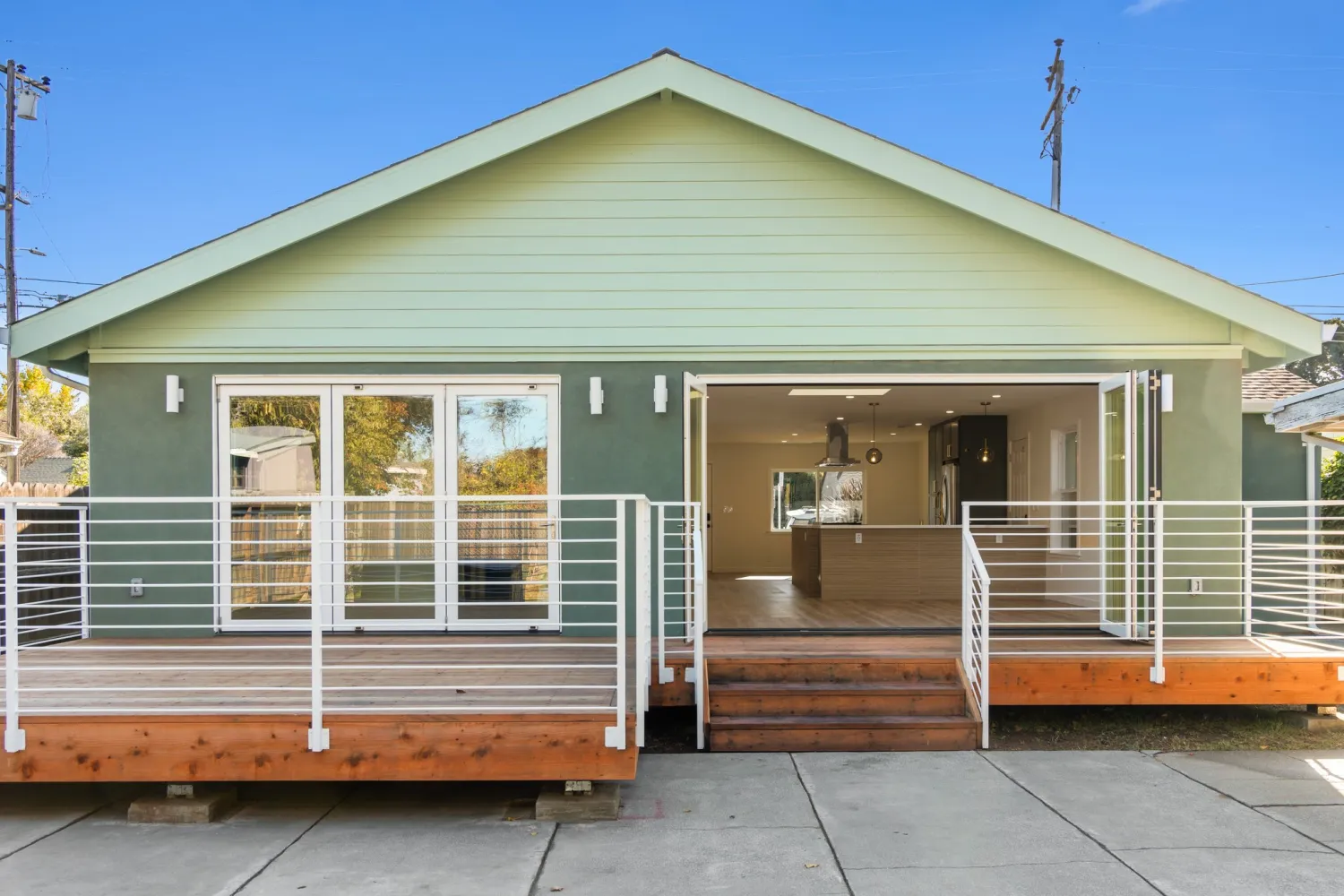 Back of the house with the new addition, a wide wood deck, white metal railings, and glass doors open to the kitchen