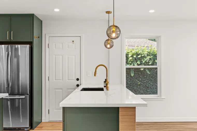 Brass gooseneck faucet at the peninsula sink next to the refrigerator and side door