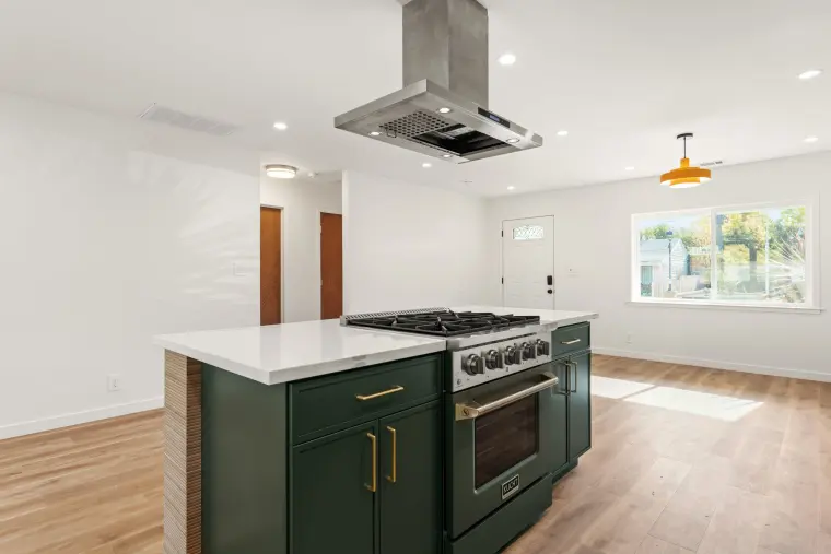 Island range under a stainless hood with the living area and front window behind