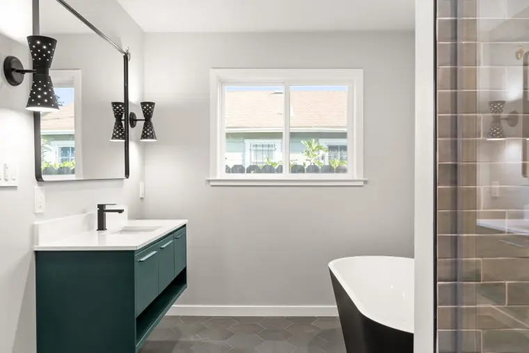 Bathroom with a floating teal vanity, black sconces, and a black and white soaking tub