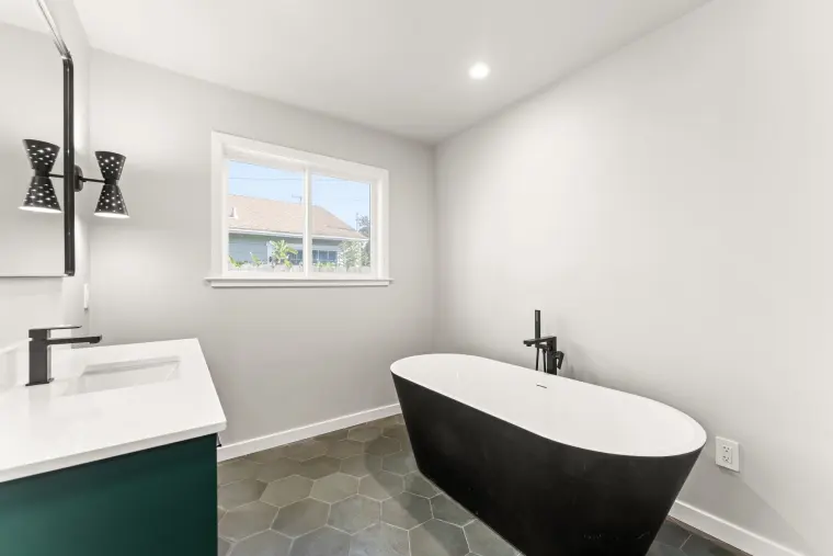 Freestanding black tub with a black floor-mounted filler on gray hexagon tile