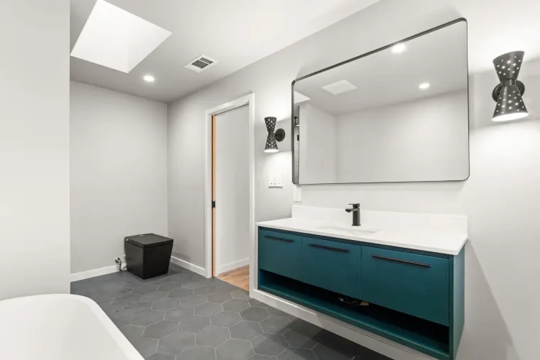 Floating teal vanity with a white top, large black mirror, and a skylight above