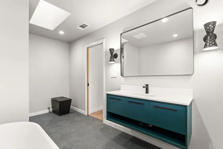 Teal vanity and black-framed mirror under a skylight