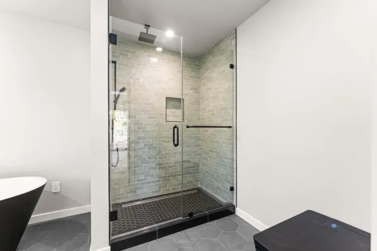 Walk-in shower with sage green tile, a black hexagon floor, and a frameless glass door
