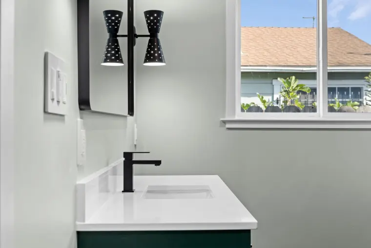 White quartz vanity top with a black faucet and sconce by the window