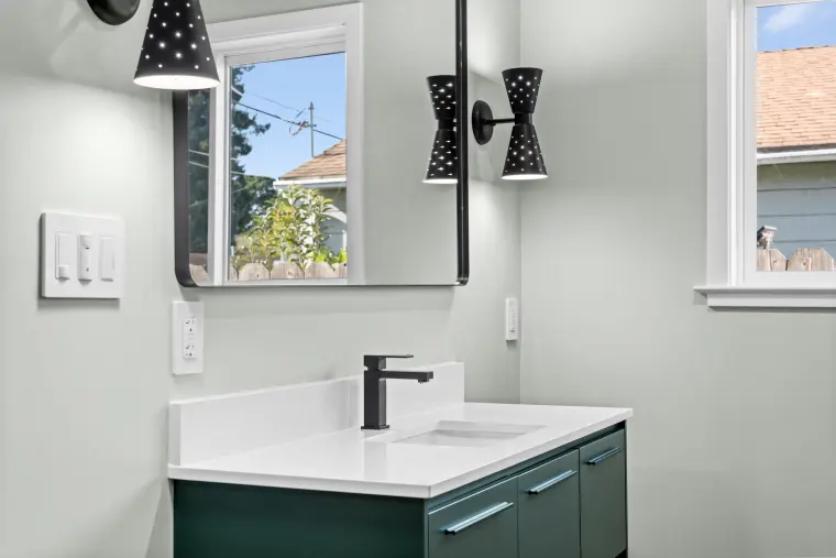 Teal vanity with a black faucet and black sconces