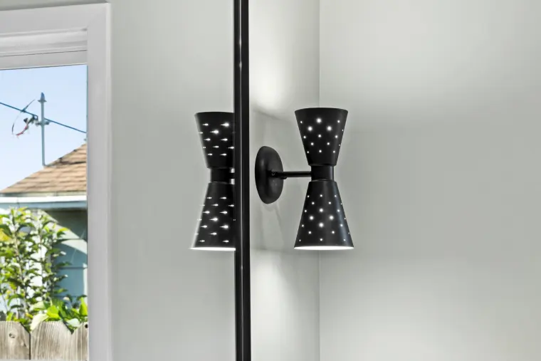 Black cone sconce with small cutouts next to the mirror
