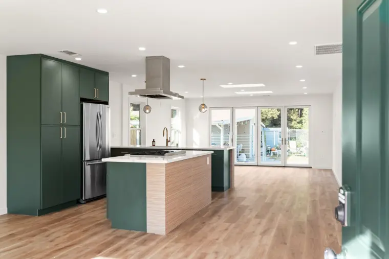 Open kitchen with green cabinets, a wood-look island, a stainless island hood, and glass doors at the back