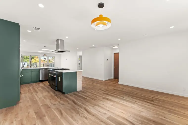 Long view through the open kitchen and living space with an orange pendant light and wood-look floors