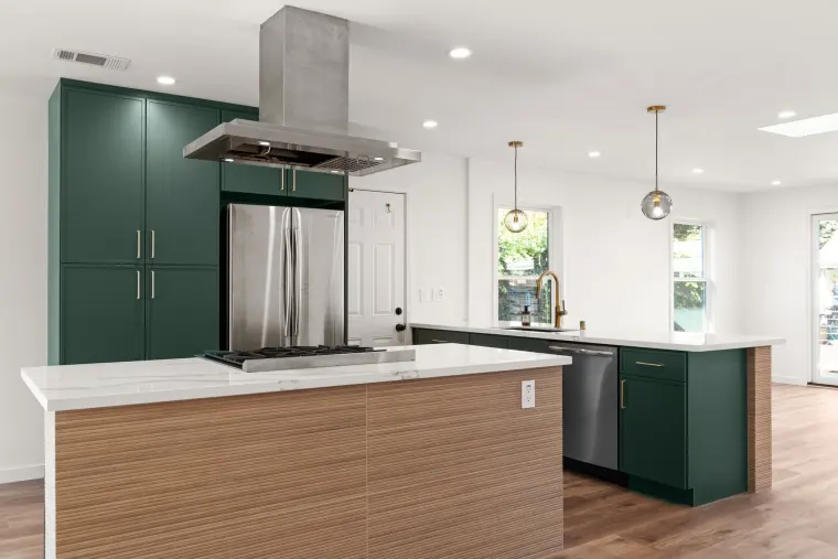 Island with a gas cooktop under a stainless hood, green tall cabinets, and a stainless refrigerator