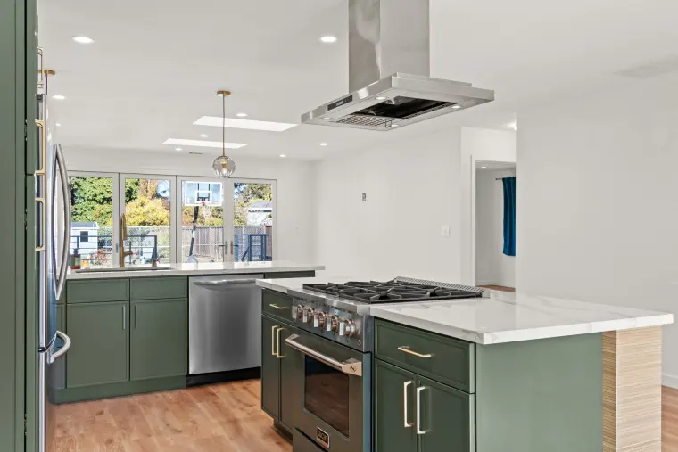 Green shaker cabinets with brass pulls around the sink wall and a stainless range in the island