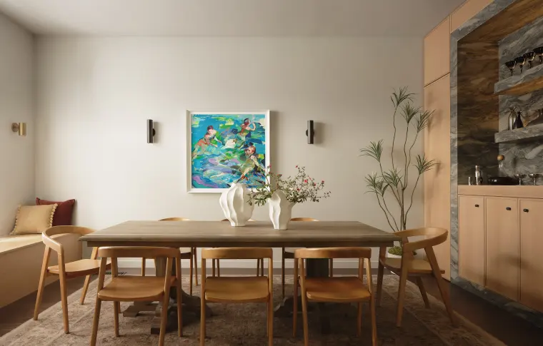 Dining room with a long wood table, a colorful painting, and a lit stone-backed bar niche
