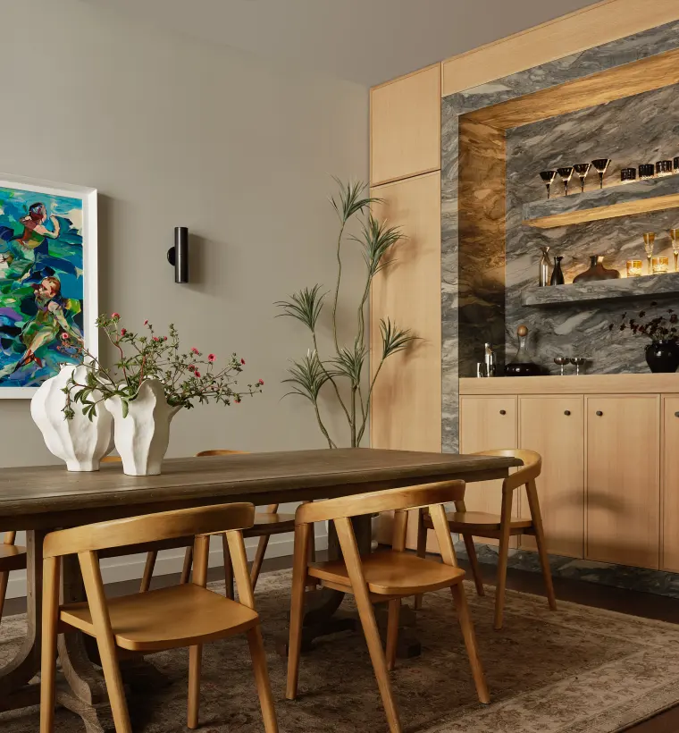 Dining table and chairs beside the built-in bar with stone backsplash and glass shelves