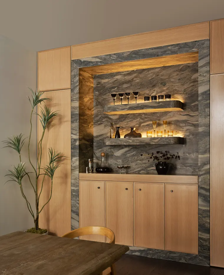 Built-in bar with a lit stone backsplash, glass shelves, and white oak cabinetry below